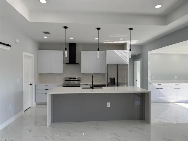 Kitchen featuring visible vents, modern cabinets, stainless steel appliances, wall chimney exhaust hood, and a sink