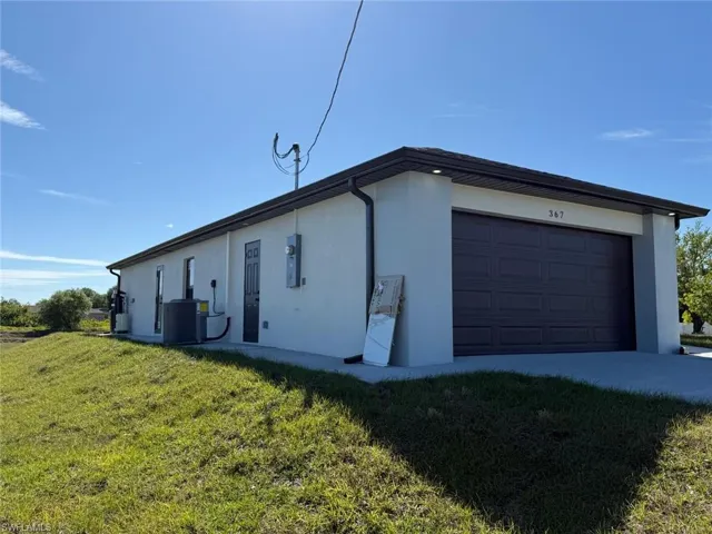 View of side of property with a yard, cooling unit, an attached garage, and stucco siding