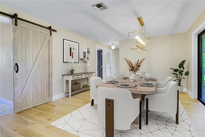 Dining space with light wood-style flooring, a barn door, and a chandelier
