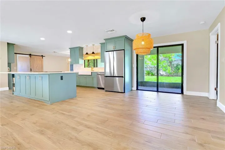 Kitchen with green cabinets, a barn door, appliances with stainless steel finishes, light countertops, and light wood-type flooring