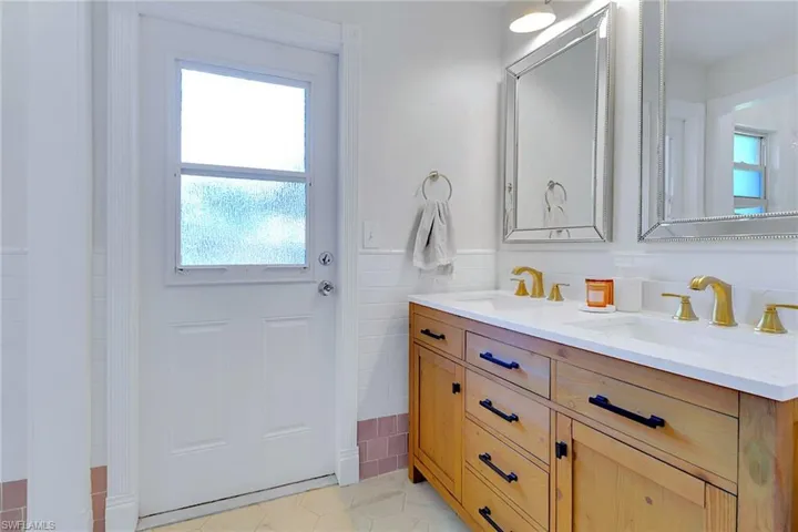Full bath featuring double vanity, wainscoting, tile walls, and light tile patterned flooring