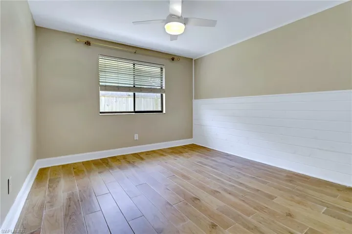 Spare room with light wood-type flooring, a wainscoted wall, a ceiling fan, and crown molding