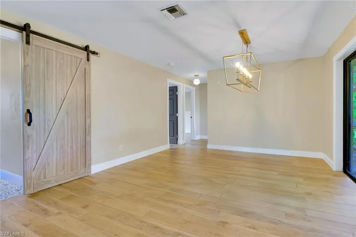 Unfurnished dining area featuring light wood-type flooring, a chandelier, and a barn door