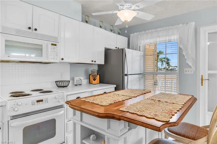 Kitchen featuring white appliances, white cabinets, a textured ceiling, decorative backsplash, and wooden counters