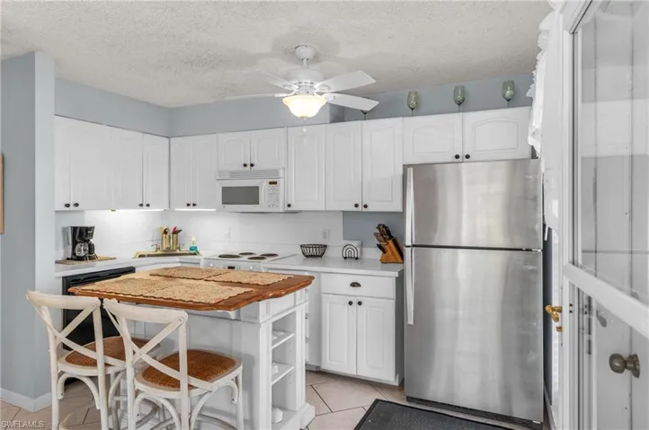 Kitchen with white appliances, light tile patterned floors, a textured ceiling, a breakfast bar area, and white cabinetry