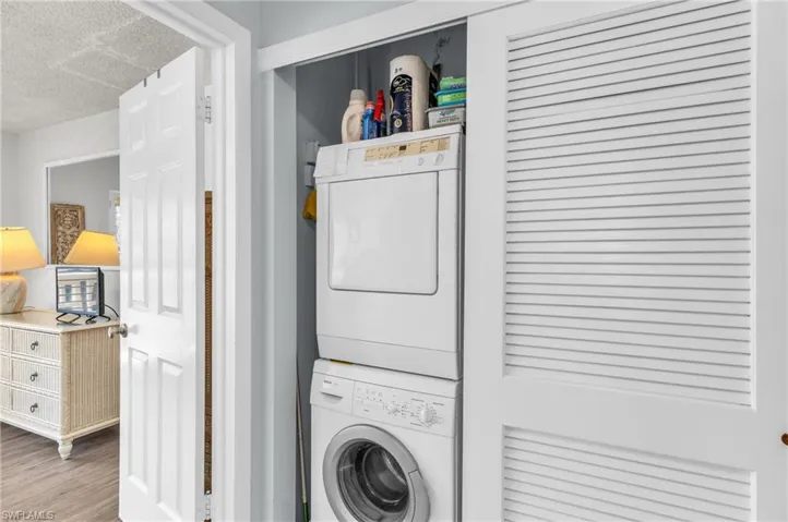 Laundry room with estacked washer and dryer, a textured ceiling, and wood finished floors