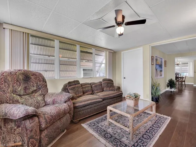 Living room with dark hardwood / wood-style floors, ceiling fan, a wealth of natural light, and a drop ceiling