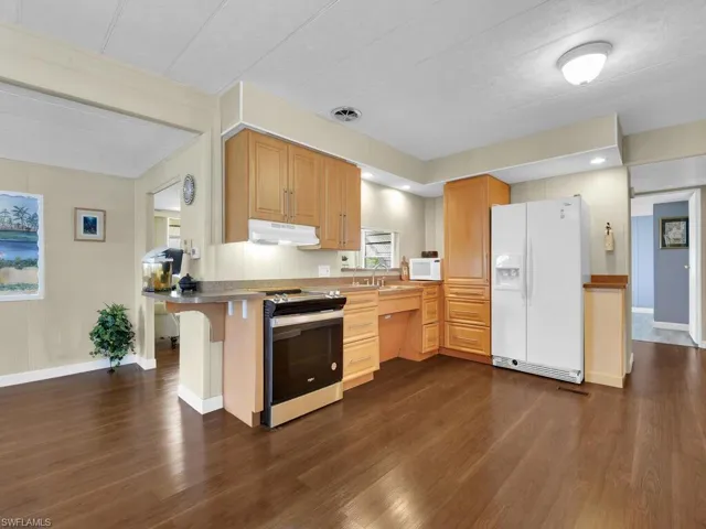 Kitchen featuring a breakfast bar, white appliances, dark hardwood / wood-style floors, and kitchen peninsula