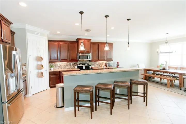 Kitchen with appliances with stainless steel finishes, a kitchen bar, hanging light fixtures, decorative backsplash, and a kitchen island with sink