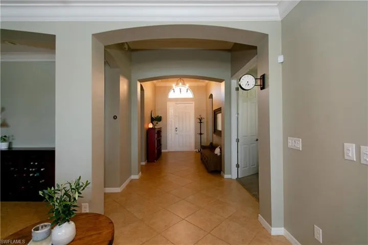 Hallway featuring arched walkways, light tile patterned floors, baseboards, and ornamental molding