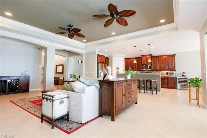 Living room featuring a tray ceiling, beverage cooler, crown molding, ceiling fan, and recessed lighting