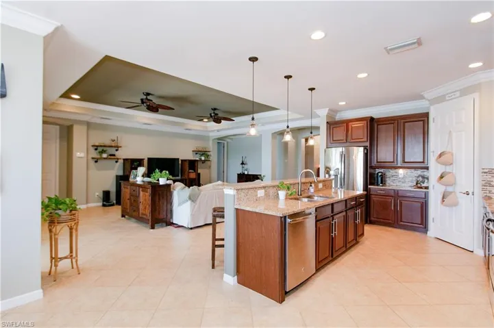 Kitchen with a kitchen bar, ornamental molding, pendant lighting, open floor plan, and a center island with sink
