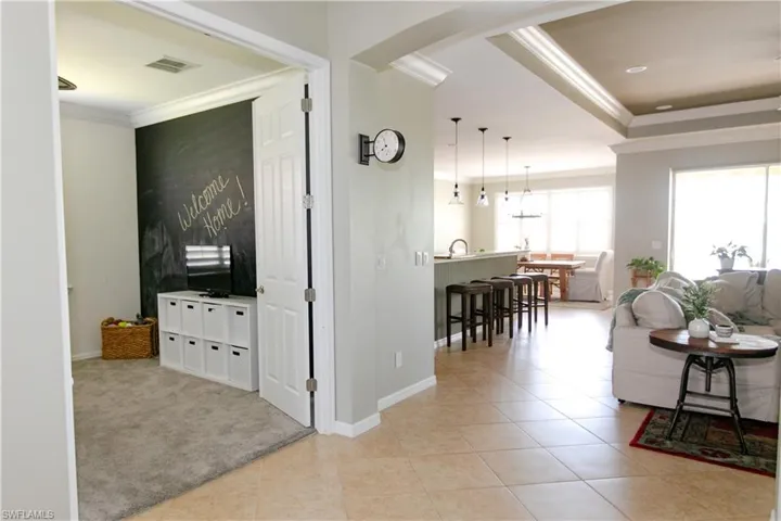 Living room with ornamental molding, light colored carpet, arched walkways, a tray ceiling, and light tile patterned floors