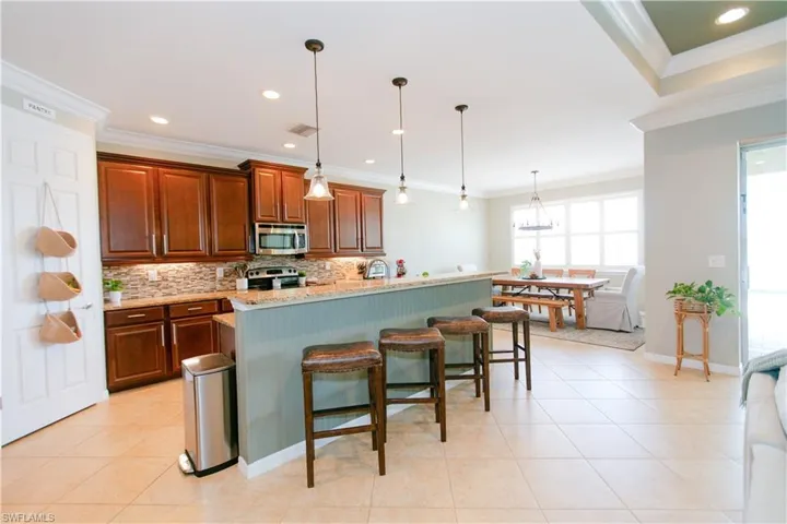Kitchen featuring a kitchen bar, decorative light fixtures, light stone counters, light tile patterned floors, and a kitchen island with sink