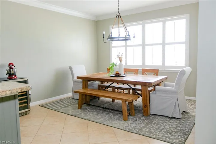 Dining area with ornamental molding, light tile patterned floors, wine cooler, and a chandelier