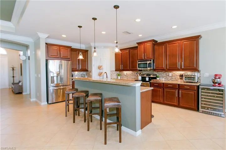 Kitchen with a breakfast bar area, appliances with stainless steel finishes, beverage cooler, hanging light fixtures, and an island with sink