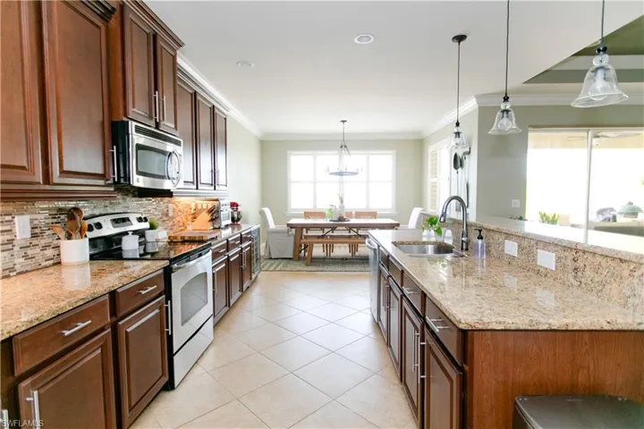 Kitchen featuring appliances with stainless steel finishes, decorative light fixtures, light stone countertops, backsplash, and ornamental molding