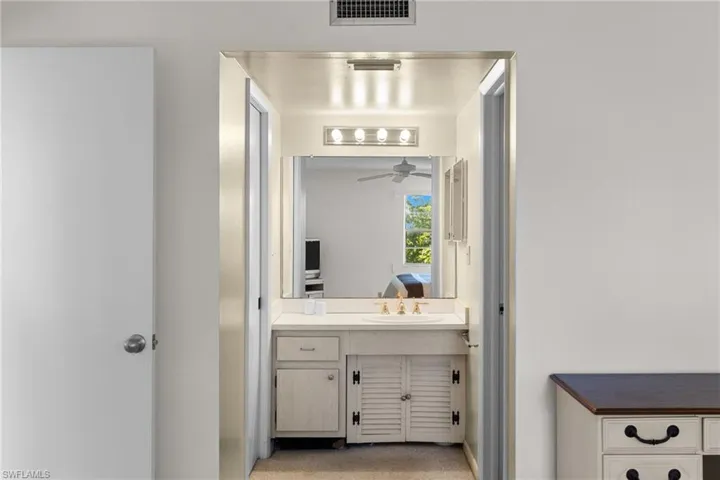Ensuite bathroom featuring vanity, light colored carpet, and ceiling fan
