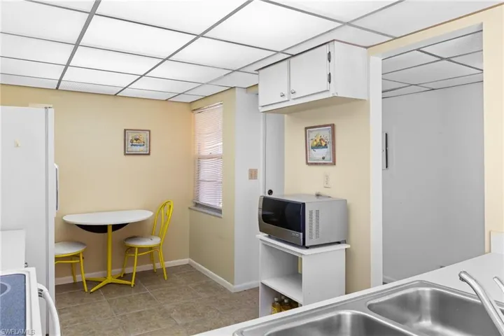 Kitchen featuring white appliances, a drop ceiling, white cabinets, light countertops, and light tile patterned floors