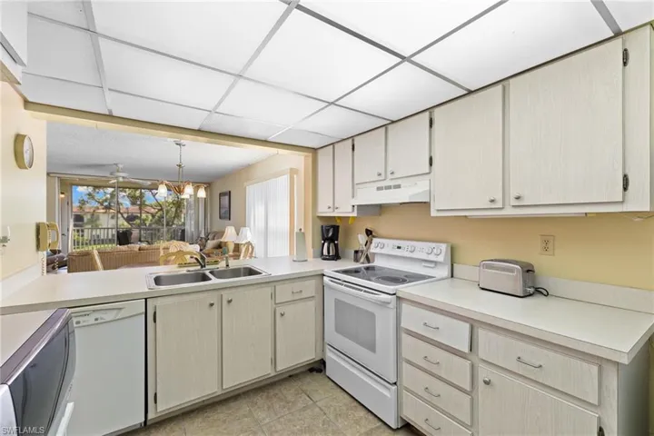 Kitchen featuring white appliances, light countertops, under cabinet range hood, pendant lighting, and open floor plan