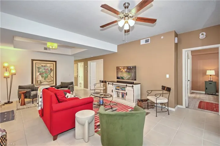 Living area with a tray ceiling, light tile patterned floors, and a ceiling fan