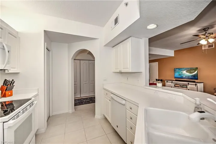 Kitchen with arched walkways, white appliances, white cabinets, light countertops, and light tile patterned flooring