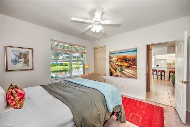 Bedroom featuring light wood-style floors, a water view, white fridge with ice dispenser, and ceiling fan