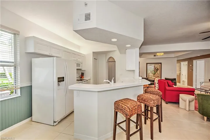 Kitchen featuring white appliances, a breakfast bar area, light countertops, light tile patterned flooring, and white cabinets