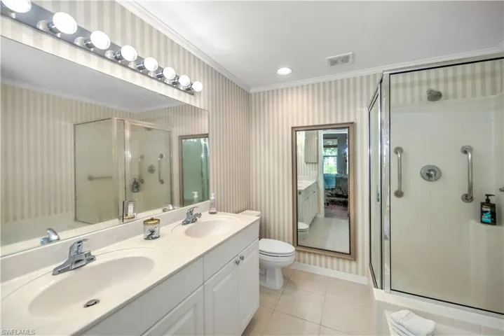 Full bathroom featuring wallpapered walls, double vanity, a stall shower, light tile patterned floors, and crown molding