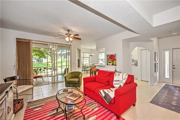 Living room with light tile patterned flooring, ceiling fan, arched walkways, and a chandelier