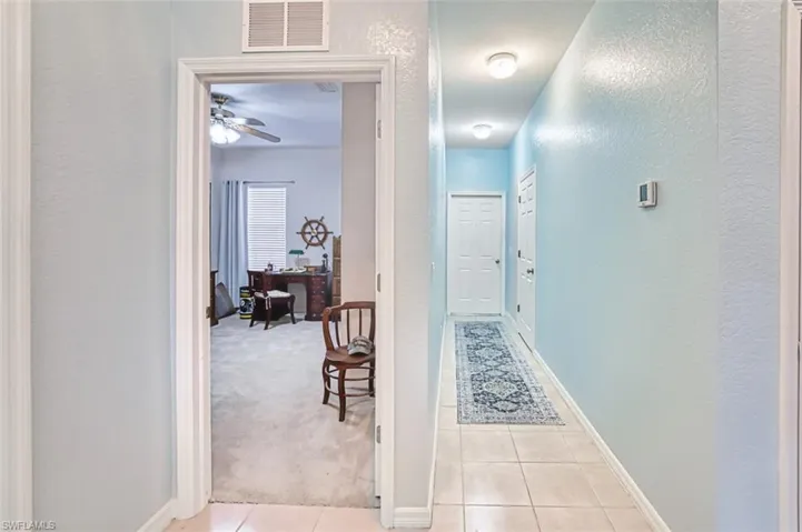 Hall featuring a textured wall, light colored carpet, and light tile patterned floors