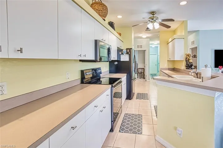 Kitchen with electric stove, a peninsula, stainless steel microwave, white cabinetry, and light countertops