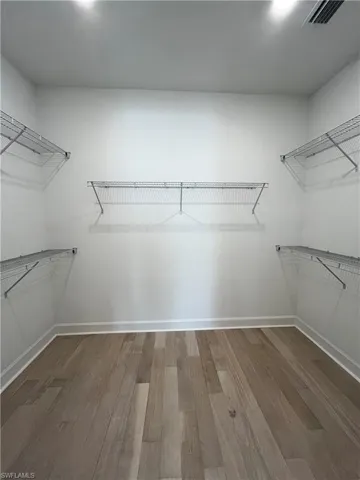 Primary walk in closet with hardwood floors