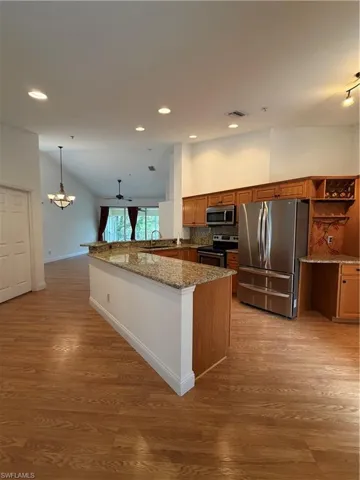Kitchen featuring dark stone countertops, wood finish cabinets, a peninsula, fridge, and stove