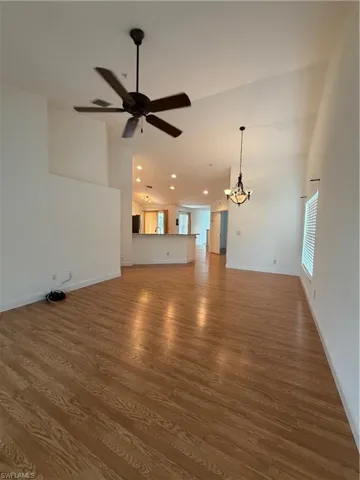 Unfurnished living room with hanging lights, dark wood-type flooring, a ceiling fan, and lofted ceiling