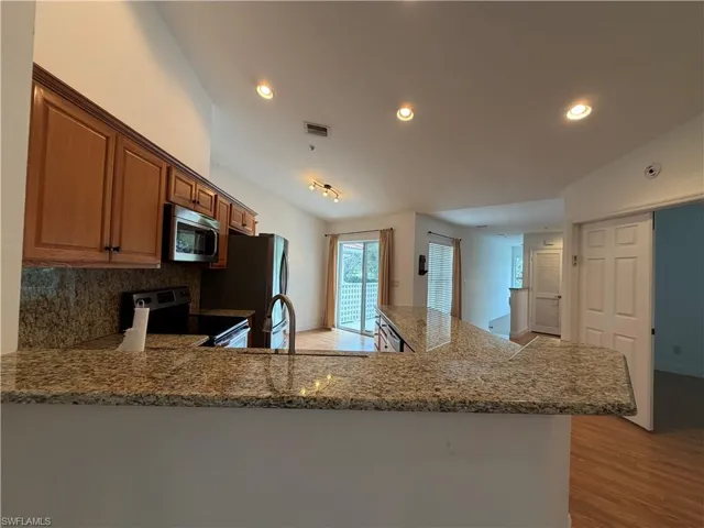 Kitchen with a peninsula, stainless steel appliances, light wood-style floors, dark stone counters, and recessed lighting