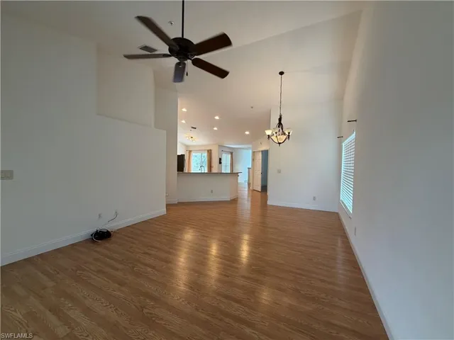 Unfurnished living room featuring a chandelier, light wood-type flooring, a ceiling fan, and vaulted ceiling