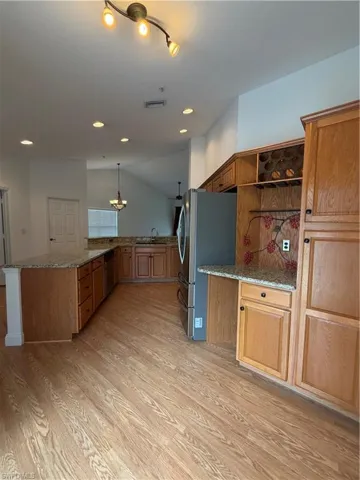 Kitchen with dark stone countertops, freestanding refrigerator, wood finish cabinets, a peninsula, and hanging lights