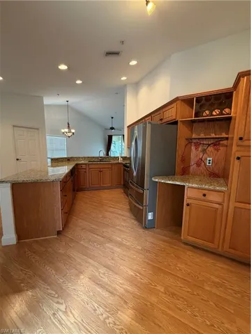 Kitchen with wood finish cabinets, light stone countertops, stainless steel fridge, vaulted ceiling, and a peninsula