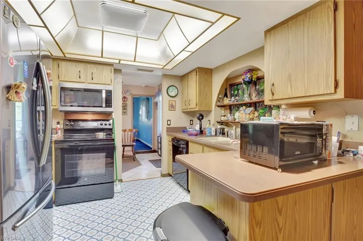 Kitchen featuring black appliances, kitchen peninsula, sink, light tile flooring, and light brown cabinetry