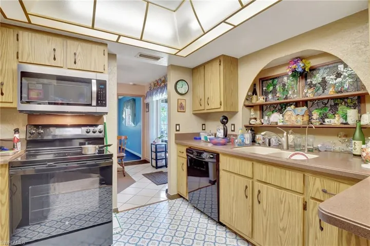 Kitchen featuring black appliances, sink, light brown cabinetry, and light tile floors