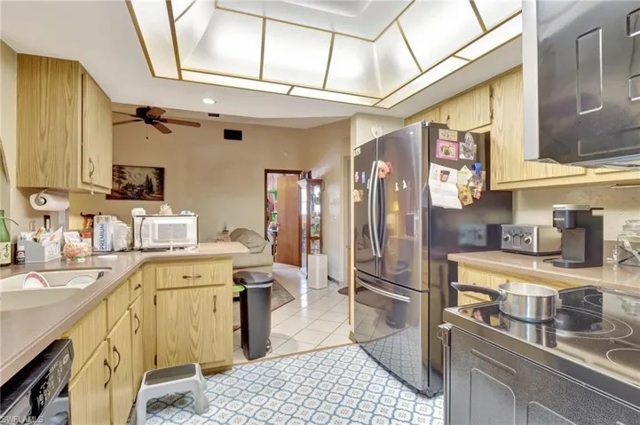 Kitchen with stainless steel fridge, dishwashing machine, light tile flooring, ceiling fan, and light brown cabinetry