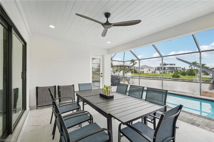 View of patio / terrace with a sunroom, a ceiling fan, an outdoor pool, glass enclosure, and a water view