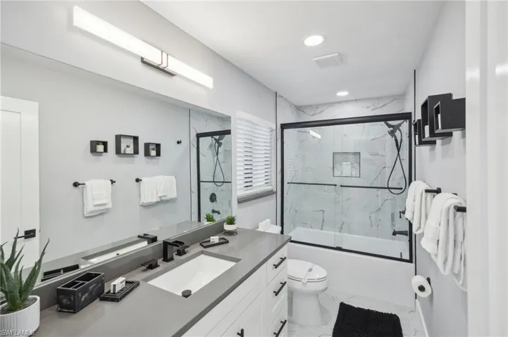 Full bathroom with enclosed tub / shower combo, vanity, light marble finish flooring, and recessed lighting