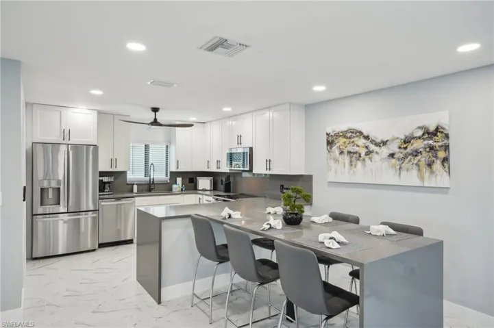 Kitchen with light marble finish floors, a kitchen bar, stainless steel appliances, tasteful backsplash, and a ceiling fan