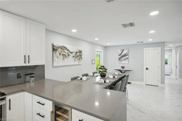 Kitchen with a peninsula, recessed lighting, light marble finish flooring, white cabinets, and beverage cooler
