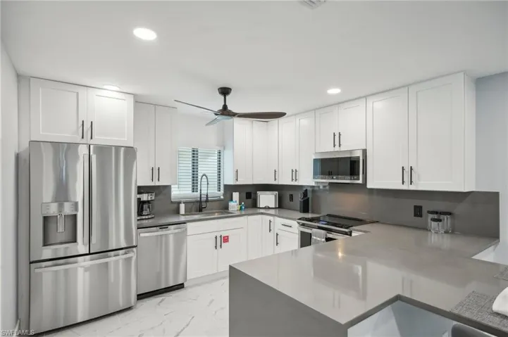 Kitchen with appliances with stainless steel finishes, backsplash, light marble finish floors, white cabinets, and recessed lighting