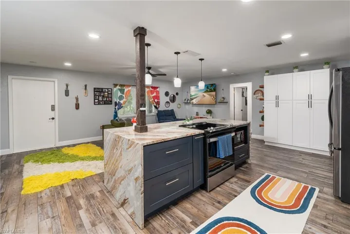 Kitchen featuring stainless steel appliances, decorative light fixtures, light stone counters, white cabinets, and hardwood / wood-style flooring