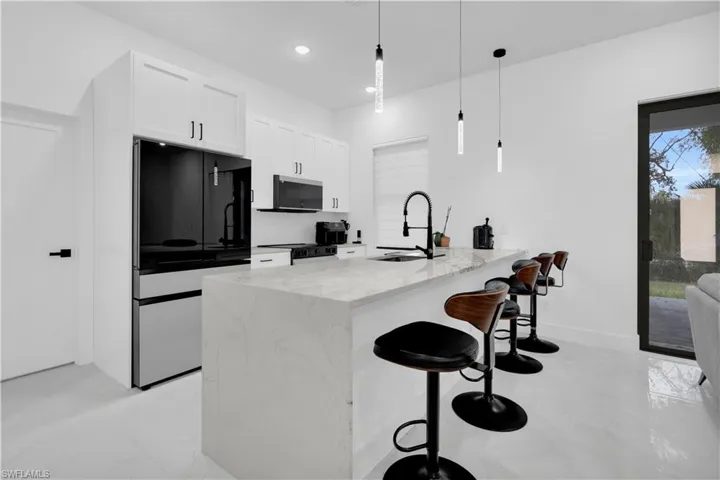 Kitchen with a kitchen bar, freestanding refrigerator, a peninsula, white cabinetry, and light stone countertops