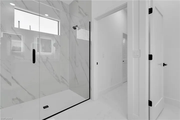 Bathroom with a marble finish shower and light marble finish flooring